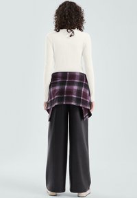 Biały prążkowany top z długim rękawem pod warstwą fioletowej koszuli w kratę, do tego szerokie czarne spodnie i beżowe buty, widziane od tyłu.