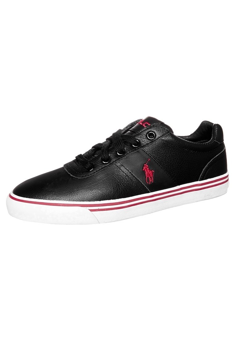 Zapatillas de cuero negro con una textura suave, que presentan un logo rojo, suela blanca con rayas rojas y blancas, y cordones redondos.