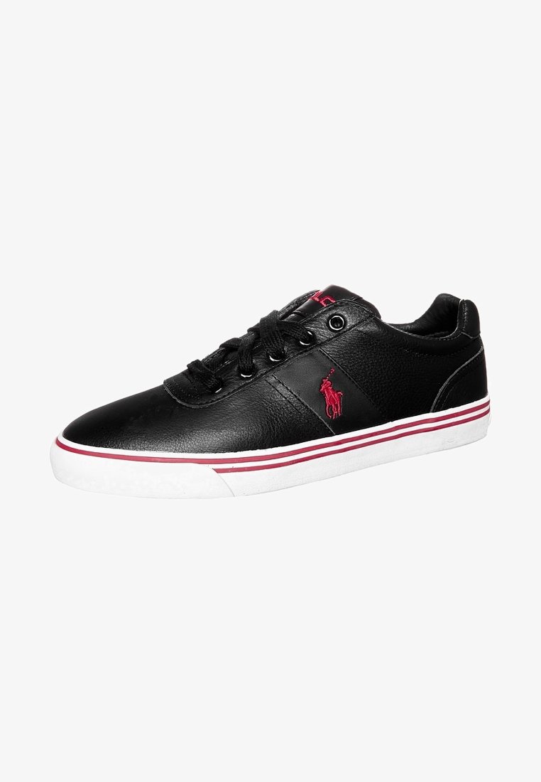 Zapatillas de cuero negro con una textura suave, que presentan un logo rojo, suela blanca con rayas rojas y blancas, y cordones redondos.