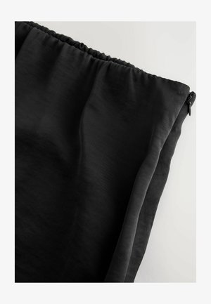 Juodas audinys su lygiu paviršiumi, elastinga juosta juosmeniui ir užtrauktuku. Medžiaga atrodo lengva ir šiek tiek permatoma.