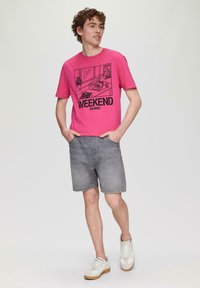 Różowa bawełniana koszulka z graficznym wzorem przedstawiającym gramofon i rośliny, w połączeniu z szarymi dżinsowymi szortami i białymi trampkami.