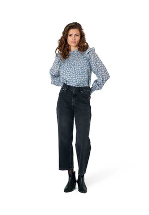 Blaue Bluse mit floralem Druck und gepufften Ärmeln, kombiniert mit hochtaillierten schwarzen Jeans und schwarzen Stiefeletten. Einfarbiger weißer Hintergrund.