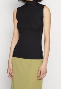 Top senza maniche di colore nero con collo alto a becco, caratterizzato da una texture a coste e un design aderente, abbinato a una gonna verde chiaro. Tessuto liscio con una leggera elasticità.
