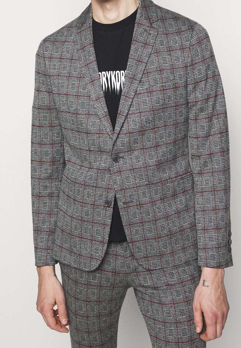 Grijze geruite blazer met rode accenten, een gestructureerde stof, gesneden revers en twee knopen. Draag het over een zwart graphic T-shirt.