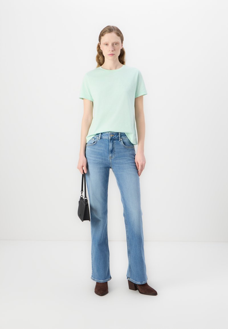 Jasnozielona bawełniana koszulka, niebieskie, dżinsowe spodnie z wysokim stanem, brązowe botki na obcasie. Czarna torebka na krótkim pasku. Minimalistyczny design.