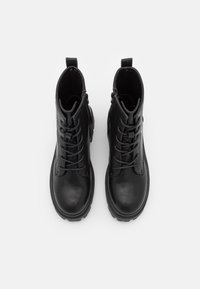 Bottines en cuir noir avec une texture lisse, bout rond, lacets à l'avant et détail de fermeture éclair sur le côté. La semelle en caoutchouc plate offre une bonne traction.