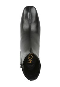 Botte de cheville en cuir noir avec un bout pointu, texture lisse, fermeture éclair sur le côté, et détail en doré sur la semelle intérieure.