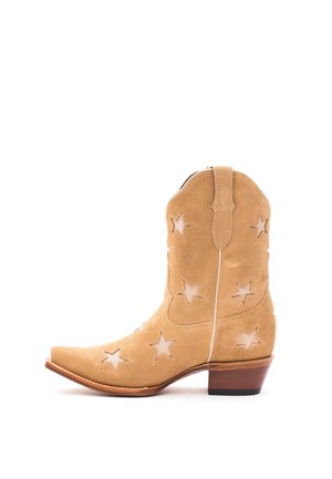 Sandfarbener Wildleder-Cowboystiefel mit sternförmigen Ausschnitten, spitzer Zehe und gestapeltem Holzabsatz, seitlich auf weißem Hintergrund gesehen.