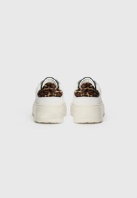 Hvite sneakers med en teksturert plattformsåle, med leopardmønster på hælen og svart detaljer. Glatt skinn og suedematerialer.
