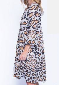 Šaty s leopardím vzorem a zvonovými rukávy, šedé pozadí, oranžové a černé skvrny, vrstevnatý design, měkká tkanina a krajkový detail.