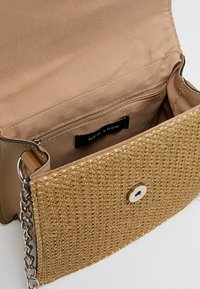 Béžová tkaná ramenní taška s klopou a magnetickým uzávěrem, béžová textilní podšívka, vnitřní zipová kapsa a stříbrný řetízek.