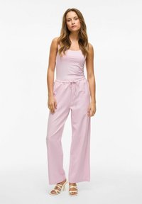Un débardeur rose clair et un pantalon à jambes larges assorti avec une taille à cordon. Tissu doux, associé à des sandales à talons carrés blanches avec des lanières.