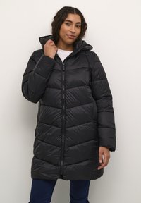 Doudoune noire avec capuche, présentant des sections matelassées, une fermeture éclair frontale intégrale et des poches latérales. Texture lisse et brillante.