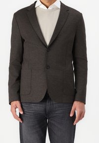 Donkergrijze blazer van gladde stof, met twee voorzakken, een enkelvoudige knoopsluiting en twee knopen. Gedragen over een lichte trui.