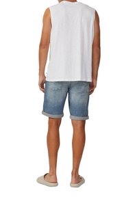 T-shirt sans manches blanche, short en denim bleu clair avec poignets roulés, chaussures légères à enfiler, vues de l'arrière.