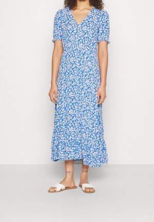 Robe midi bleue à motifs floraux avec un col en V et de courtes manches bouffantes. Fabriquée en tissu léger, elle présente une jupe à volants. portée avec des sandales blanches.