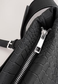 Melnas teksturētas somas ar rāpuļu rakstu, gludām ādas detaļām un sudraba rāvējslēdzēja akcentu. Siksna redzama sānos.