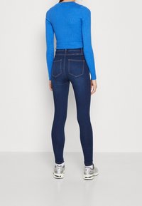 Blauses, geripptes Langarmoberteil in Blau, kombiniert mit hoch taillierten, dunkelblauen Skinny Jeans, die über Gesäßtaschen und eine glatte Textur verfügen.