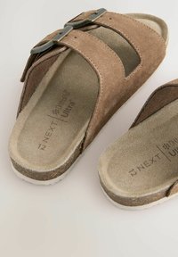 Bruna mockasteg-sandaler med en dubbelremdesign, försedda med en dekorerad metallspänne och en dämpad fotbädd. Inkluderar texturerade sulor.