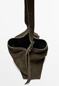 Suede tote bag in olive green with a zip closure, adjustable strap, and black interior. Features a knotted detail at the base.