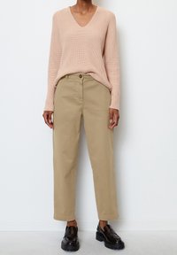 Pull côtelé rose clair avec col en V, assorti à un pantalon beige à jambes droites et des mocassins noirs à semelles épaisses. La tenue présente une coupe décontractée.