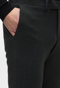 Pantaloni tailleur grigio scuro con texture liscia, dotati di tasca laterale e passante per cintura in vita. Linee di design pulite.
