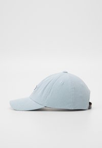 Casquette en velours côtelé bleu clair avec unvisière proéminente, logo brodé à l'avant et une sangle ajustable marron à l'arrière.