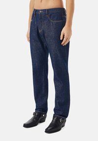 Mörkblå denimjeans med lös passform och synliga sömnadsdetaljer. Kombineras med svarta läderstövlar med klack och spännvidd.