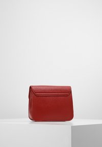 Červená kožená kabelka se strukturovaným tvarem, hladkou texturou a klopovým uzávěrem. Na povrchu má jemný diagonální vzor.