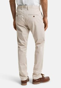 Pantalones de algodón color caqui con un diseño de pierna recta, que cuentan con dos bolsillos traseros con botones marrones y una textura suave. Llevados con zapatos marrones.