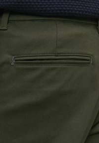 Pantaloni verzi măslinii cu o textură netedă, având un buzunar cu captuseală pe spate, cu cusături îngrijite. Design clasic și croit.