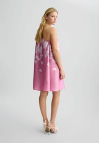 Abito senza maniche di colore rosa con un motivo floreale bianco. Presenta una vestibilità comoda e arriva sopra il ginocchio. Indossato con tacchi a strappo.