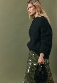 Black fluffy knit sweater, green sequined skirt, and a black beaded handbag. The outfit features textured materials and accentuated shapes.