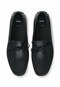 Czarne skórzane mokasyny z okrągłym noskiem, związywane z przodu i z detalicznym przeszyciem. Wyściełane wnętrze, logo nadrukowane na wkładkach.