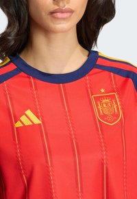 Punane jalgpallisärk kollaste detailidega, mis kannab Hispaania rahvusmeeskonna vappi ja Adidas logo, ümmargune krae ning kangal triibutis.