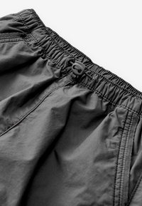 Pantaloni corti neri con vita elastica in tessuto leggero, caratterizzati da una chiusura con cordino e tasche laterali, con una texture liscia e dettagli di cucitura minimali.