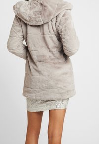 Lys beige faux fur frakke med hætte, quiltet design og en blød tekstur, parret med en skinnende paliet mini nederdel.