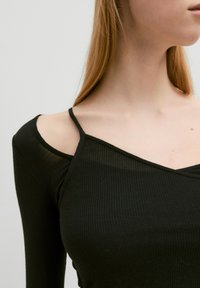 Schwarzes, geripptes Langarmoberteil mit tiefem V-Ausschnitt und dünnen Schulterträgern, das eine leichte Transparenz des Stoffes zeigt.