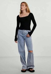 Μαύρο ριμπ μακρυμάνικο μπλουζάκι με τετράγωνη λαιμόκοψη, συνδυασμένο με ανοιχτό μπλε ψηλόμεσα τζιν με κοψίματα στα γόνατα, φορεμένο με μαύρες σαγιονάρες.