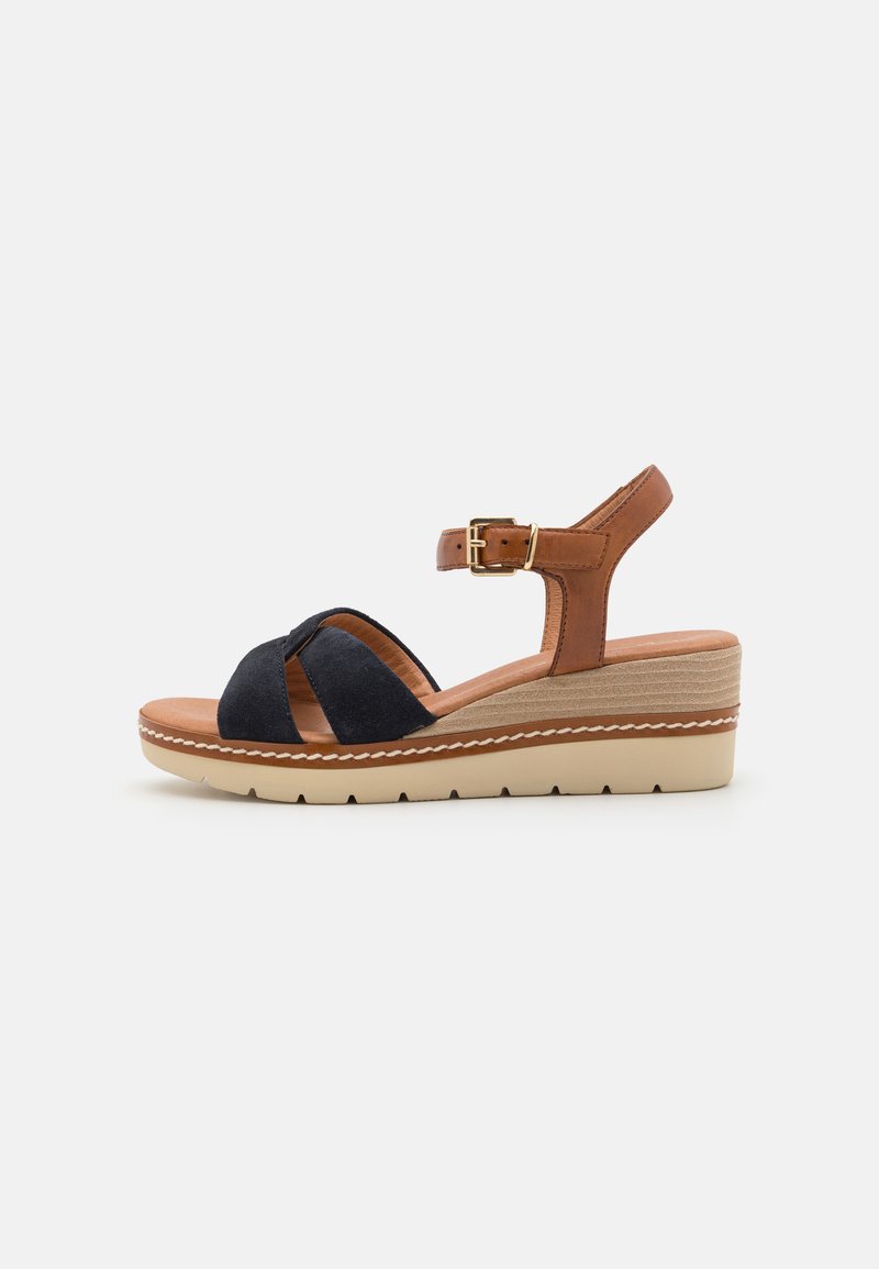Wedge sandal with navy suede upper and tan leather straps, adjustable buckle, beige wedge sole with stitched accents and textured bottom.