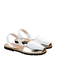 Sandalias metálicas plateadas con punta abierta y dos correas ajustables. Cuenta con una suela negra plana y una plantilla color tostado para mayor comodidad.