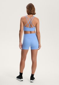 Sutien sport de culoare albastru deschis și pantaloni scurți asortați, cu bretele încrucișate și talie înaltă; textură netedă cu detalii ale logo-ului pe ambele piese.