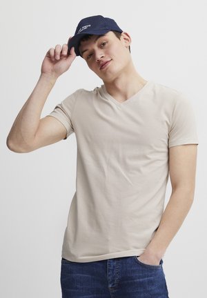 T-shirt en coton beige à col en V associé à une casquette bleu marine. Le t-shirt possède des manches courtes et une texture lisse. La casquette présente des détails brodés.