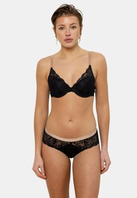 Soutien-gorge en dentelle noire avec des bonnets rembourrés et des bretelles transparentes ; le culotte en dentelle noire assortie possède une taille nude. Texture du tissu lisse.