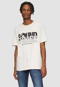 Lichtbeige katoenen T-shirt met gedurfde zwarte "SOUNDTRACK" grafiek en accent van een vinylplaat. Relaxte pasvorm en korte mouwen.