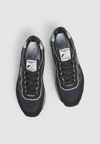 Black athletic shoes with lace-up design, mesh and synthetic upper, silver accents, and a patterned sole. Dual branding on tongue.