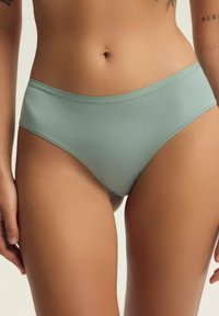 Para jasnooliwkowych, bezszwowych majtek, charakteryzujących się gładką teksturą i krojem typu slip. Pasek jest minimalistyczny i znajduje się tuż nad biodrami.