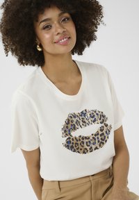 T-shirt blanc à manches courtes avec un graphique de lèvres en imprimé léopard dans des tons marron, noir et bleu. Tissu en coton lisse, coupe décontractée.