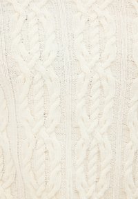 Sweter z splotem w kolorze kremowym, z teksturowanym wzorem z przekręconych sznurków. Materiał wydaje się miękki i przytulny, o grubym fasonie.