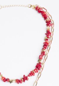 Collana di perline rosse con pietre simili al corallo e anelli in metallo dorato, inclusi accenti esagonali e a forma di stella, con chiusura a moschettone.